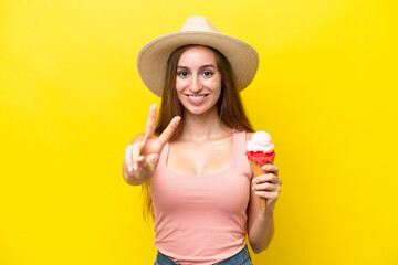 Young caucasian with a cornet ice cream isolated on yellow background smiling and showing victory...