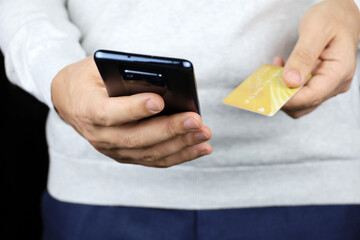 Man in sweater holding smartphone and credit card in hands. Concept of online payments, shopping and transactions