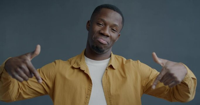 Slow motion portrait of happy African American man pointing down asking to subscribe recommending content on grey color background