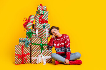 Full length photo of lovely cheerful woman wear ornament sweater sit near presents look empty space isolated on yellow color background