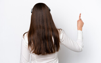 Telemarketer caucasian woman working with a headset isolated on white background pointing back with the index finger