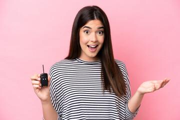Young Brazilian woman holding car keys isolated on pink background with shocked facial expression