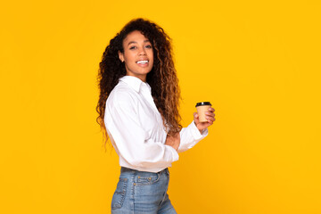 african american lady holding paper coffee cup on yellow background