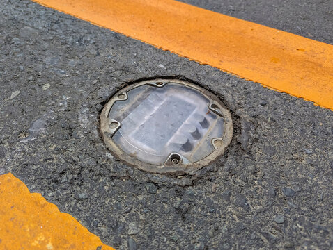 Daytime view of recessed solar road stud markers embedded in the center lane of an asphalted highway. Also known as a road reflector.