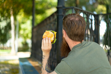 Redhead man with beard holding a burger at outdoors in back position