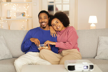 Black husband and wife engrossed in online film, snuggling indoor