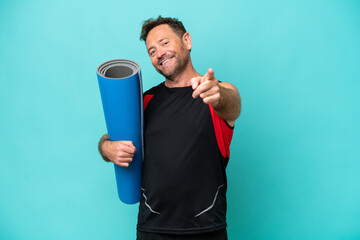Middle age sport man going to yoga classes while holding a mat isolated on blue background pointing...