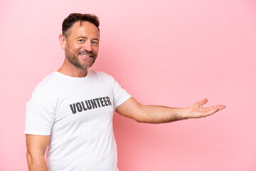 Middle age volunteer man isolated on pink background isolated on pink background extending hands to the side for inviting to come - obrazy, fototapety, plakaty