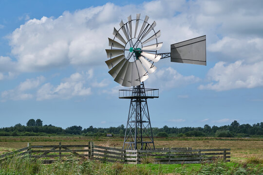 An american wind engine against a blue sky with clouds in a rural area.