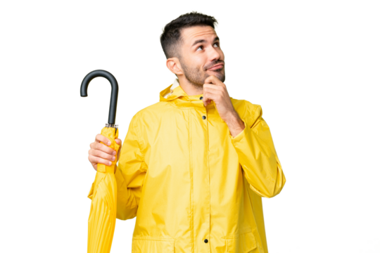 Young caucasian man with rainproof coat and umbrella over isolated background having doubts