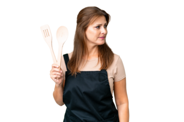 Middle age caucasian woman holding a rolling pin over isolated background looking to the side