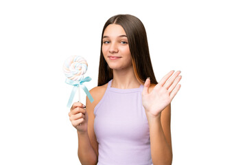 Teenager caucasian girl holding a lollipop over isolated background saluting with hand with happy expression