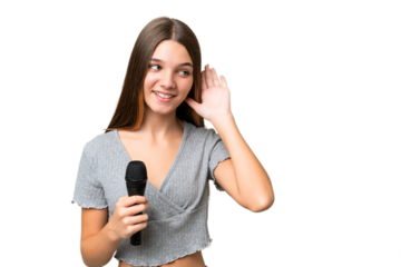 Teenager singer girl picking up a microphone over isolated background listening to something by putting hand on the ear