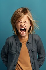 Angry irritated girl. Full of rage. Emotional portrait of an upset preteen boy screaming in anger. Requirements for parents. Wrong perception. Hysterics. Photo on blue background.
