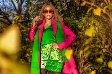 Beautiful woman wearing a pink elegant coat and green scarf is posing outdoors on a sunny autumn day.