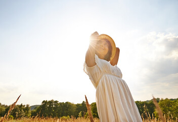 Thinking, relax and woman with sunshine, countryside and nature with grass, vacation and outdoor. Person, holiday and girl with lens flare, dress and sustainability with confidence, energy or freedom