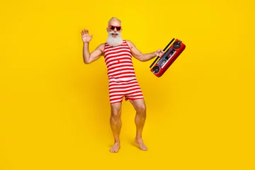 Tuinposter Full length photo of funky old man wearing striped overalls holding vintage boombox at terrace isolated on yellow color background © deagreez