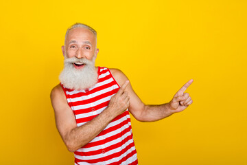 Photo of funky excited senior man wear red striped swimsuit pointing two fingers empty space isolated yellow color background