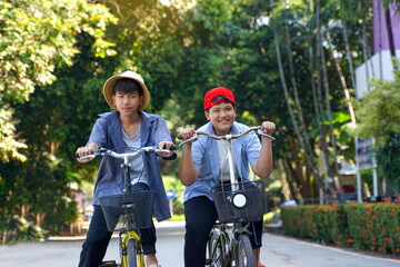 Obraz premium Two Asian boys who are friends ride bicycles in the local park on holiday. They are both happy and having fun. Holiday activity concept. Soft and selective focus.