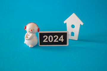 Snowman poses with the number 2024 on wooden board on new year's eve against the of a miniature...