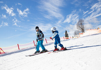 llittle boy learning to ski with his father during winter holidays in snowy mountains on a sunny...