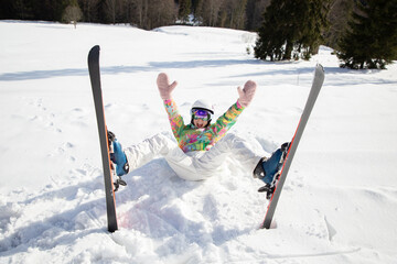 young woman or teenage girl in good mood while skiing fell and lies cheerfully in the snow....