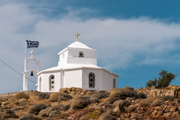 Fototapeta na wymiar A quaint Greek chapel stands proudly on the cliff's edge, its flag fluttering in the sea breeze, offering a picturesque and spiritual view of Greece's coastal beauty.