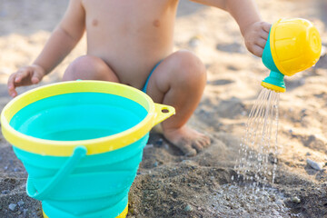 cute adorable baby boy kid is playing on beach with bucket and toy watering can.child with sun hat cat on head on seashore.sea waves summer vacation time.sunshine of face,warm weather