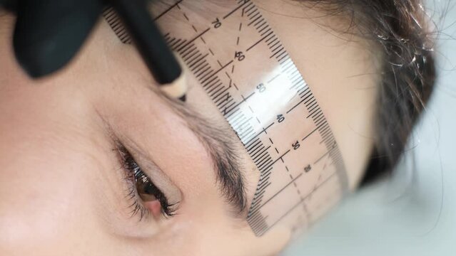 A woman in gloves prepares for permanent eyebrow makeup with a ruler. Close-up.