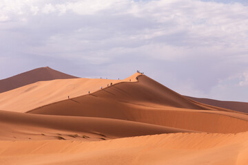 Fototapeta na wymiar Unrecognizable people climbing a red dune near Deadvlei, Sossusvlei, Namibia