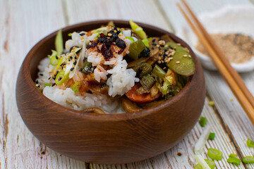Vegan rice and vegetable stir fry in wooden bowl on white wood table. Chopsticks, restin on a small plate with sesame seeds