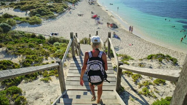 backpacker tourist girl descending the steps to Pinky Beach of Bathurst Lighthouse. Turquoise sea and white pristine beach in north coast of Rottnest Island of Perth, Western Australia.