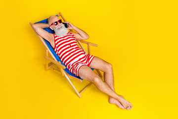 Full length portrait of carefree aged man sunbathing lounger speak telephone isolated on yellow color background