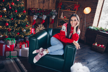 Photo portrait of pretty brunette young girl sit soft armchair enjoy comfort wear ornament sweater beautiful living room decor christmas