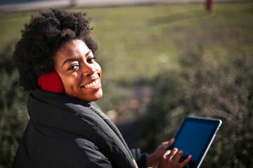 young black woman uses a tablet in a park