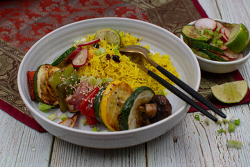 Vegan vegetable skewers with yellow rice in a white bowl. Stylish table setting.