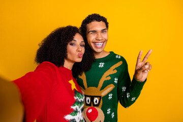 Photo of flirty funky guy girl dressed christmas ugly print pullovers showing v-sign recording video vlog isolated yellow color background