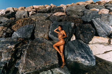 A beautiful young, sensual woman in a swimsuit is lying on the rocks by the sea.