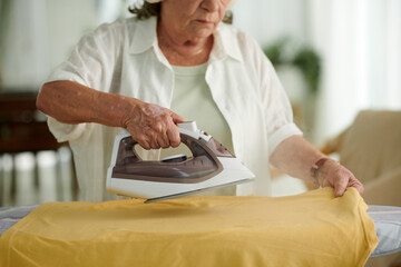 Cropped image of aged woman steaming tshirt on board