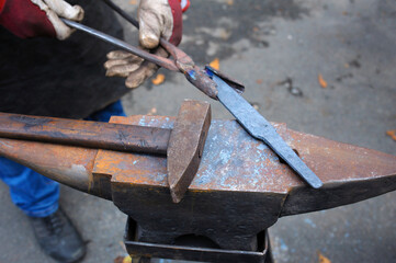 Blacksmith hands holding forceps and a hammer forging a metal billet blade of a knife on an anvil