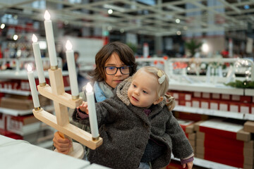 Teenager boy with little toddler girl looking at Christmas decorations in a large supermarket. Children waiting for New Year, preparation for winter holidays. High quality photo