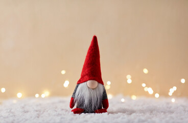christmas, decoration and winter holidays concept - close up of gnome toy on artificial snow over lights on beige background