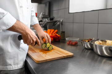 cooking food, profession and people concept - close up of male chef with knife chopping cucumber on cutting board at restaurant kitchen