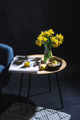 interior, holidays and home decor concept - close up of modern blue chair, easter eggs in bowl and daffodil flowers on table in dark room