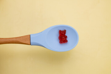 Gummy vitamins, gummy bear in a blue spoon on yellow background.