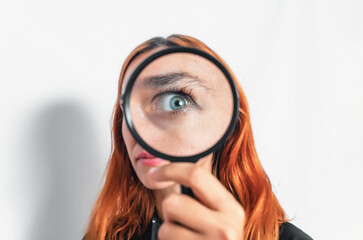 Inquisitive girl with red hair looking through magnifying glass, lens