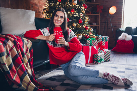 Photo of pretty cheerful girl sitting on floor fluffy carpet holding cup enjoying weekend day winter vacation decorated room indoors