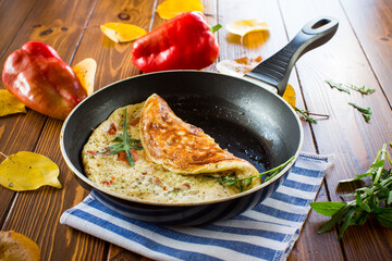 Fried omelets with various autumn vegetables in a frying pan on a wooden table.