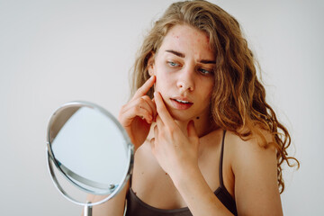 Dermatology. A beautiful woman looking in the mirror, touching her face with her hand, examines...