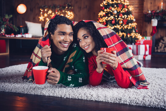 Photo of two idyllic partners laying carpet floor under warm blanket drink hot chocolate cozy festive christmas atmosphere indoors